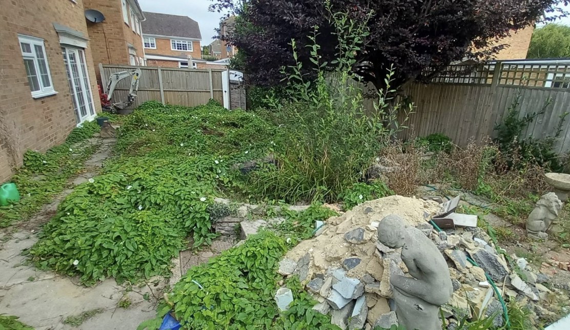 Overgrown jungle garden with rubble and a digger before clearance in Kent